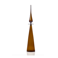 The Cariati Petite Decanter Straight Cone is a tall, slender handblown amber glass decanter with a sharp flame-like stopper—a striking modern barware piece.