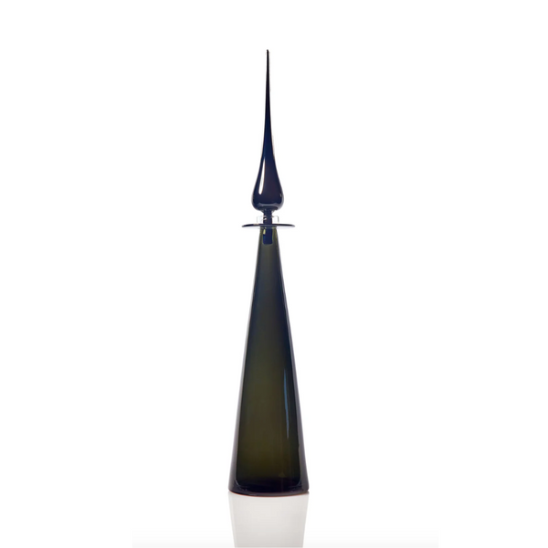 The Cariati Petite Decanter Straight Cone features a tall, slender dark glass body with a long, pointed stopper and minimalist design, making it a striking piece of modern barware against a white background.