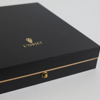 A close-up of a black rectangular box with platinum accents displays the L'Objet logo and name in platinum on the lid. Made to hold the Deco Twist Platinum Frame, it features a small platinum clasp on the front.
