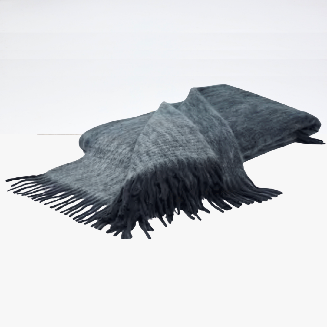The Diana Mohair Throw by Mantas Ezcaray, in soft gray mohair with fringed edges, is folded and draped on a white surface, adding an elegant touch.