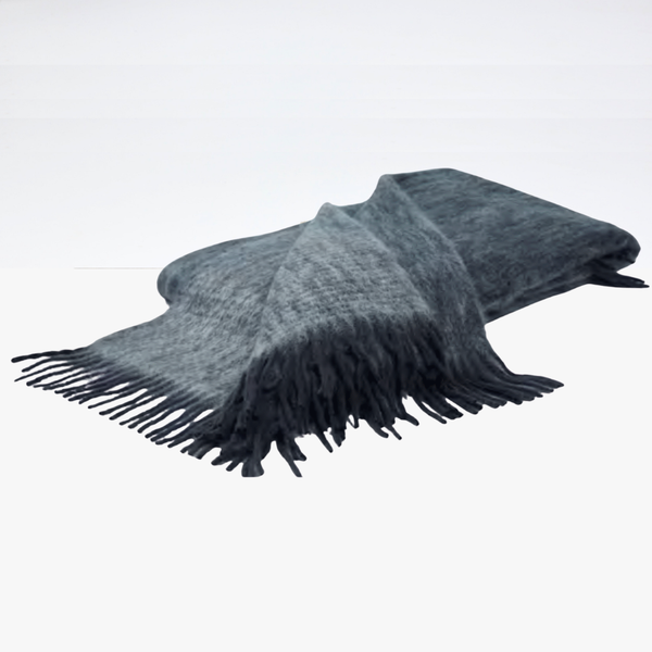 The Diana Mohair Throw by Mantas Ezcaray, in soft gray mohair with fringed edges, is folded and draped on a white surface, adding an elegant touch.