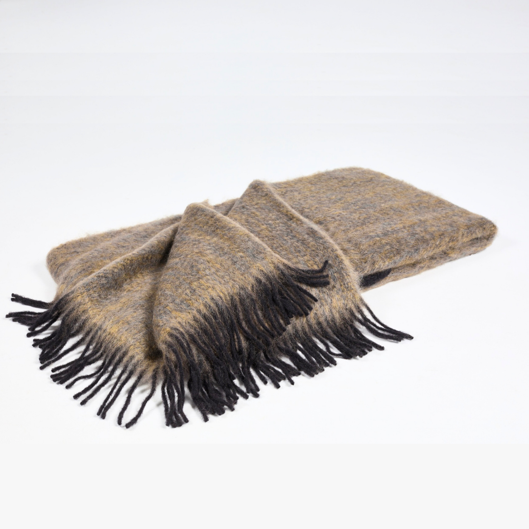 The Diana Mohair Throw by Mantas Ezcaray is a folded brown and gray blanket with long dark fringes, made from fine mohair wool and elegantly displayed on a plain white background.