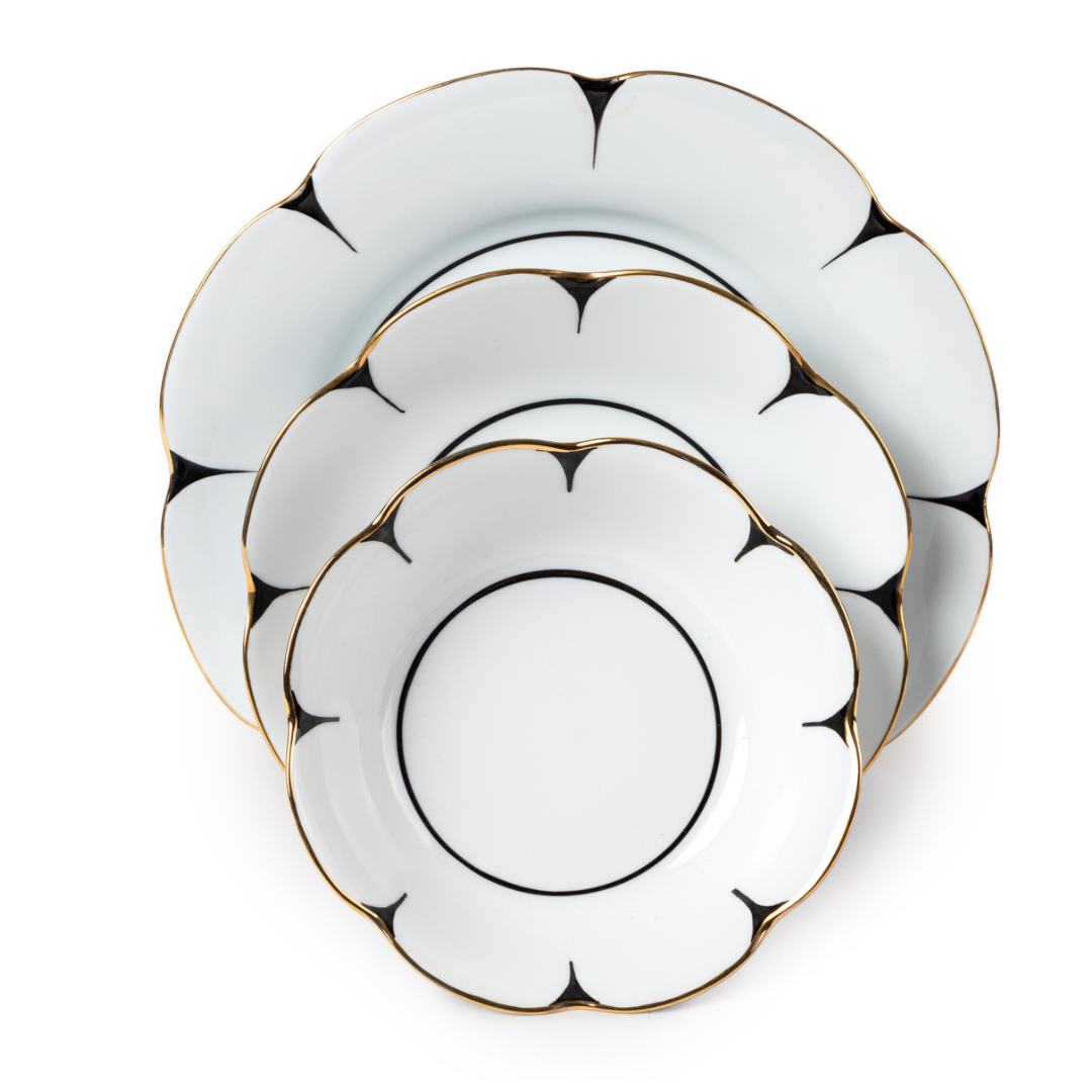 Three white Drops Dinnerware plates by Molecot, made of Limoges porcelain with scalloped, flower-shaped edges and gold trim, are stacked from largest to smallest. Each plate has a simple black accent near the rim.