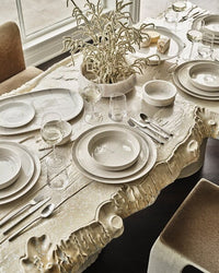 The Serax Dune Oval Platter Alabaster -18" is the centerpiece of a modern table set for six, featuring layered white tableware, sleek glasses, silverware, and a dried botanical arrangement.