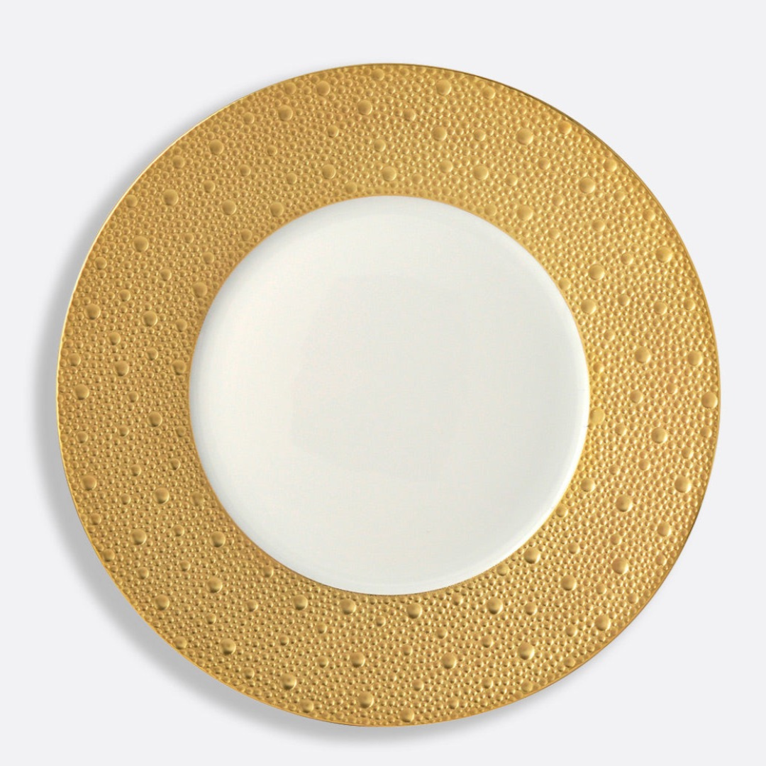 The Ecume Dinnerware Gold by Bernardaud is a white porcelain plate with a wide, textured gold rim adorned with raised dots—a sophisticated Limoges piece showcasing contemporary tableware design.