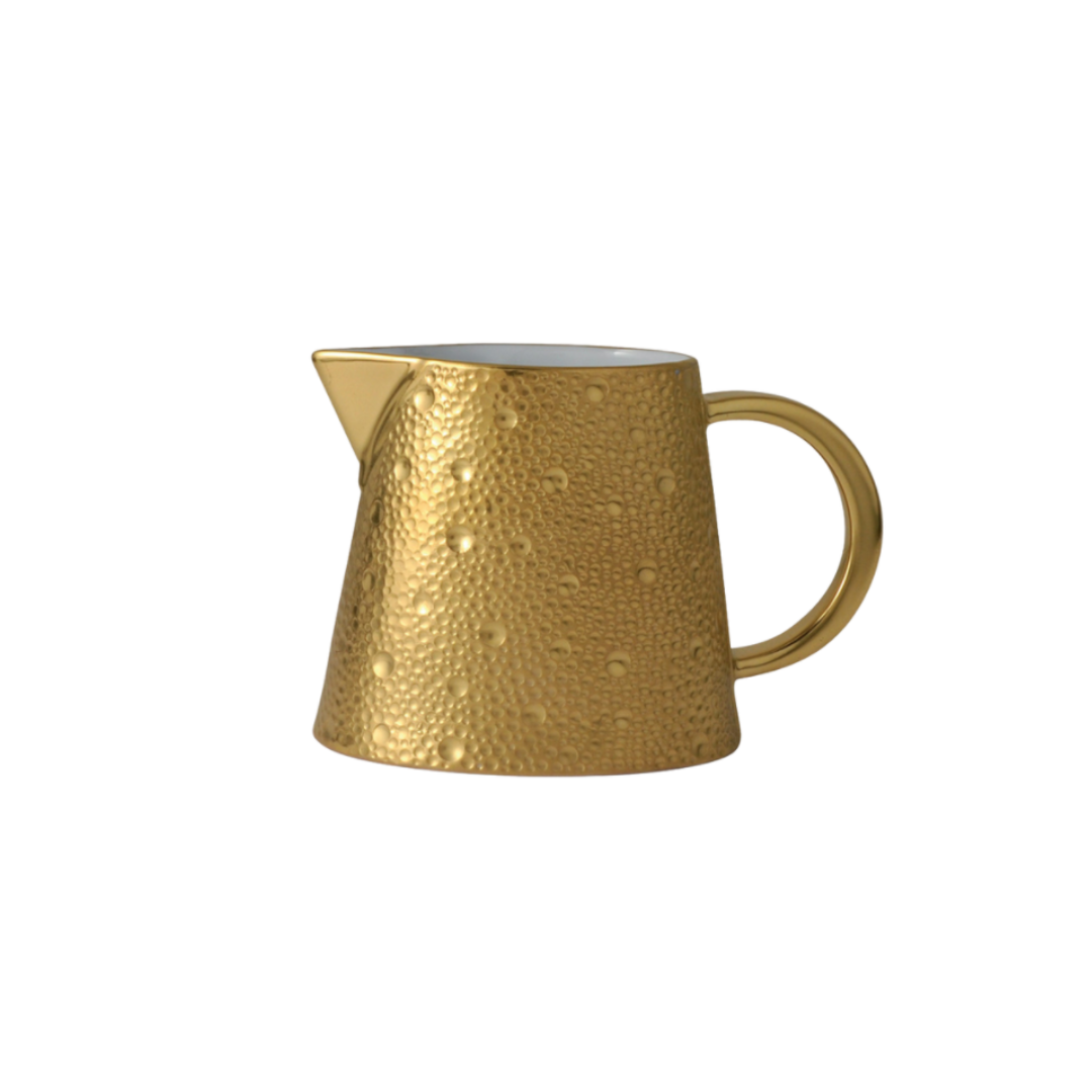 The Ecume Dinnerware Gold by Bernardaud is a small, gold, textured ceramic pitcher with a round handle and pointed spout, shown against a plain white background.
