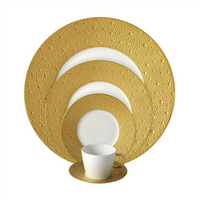 A set of Bernardaud Ecume Dinnerware Gold—white porcelain with textured gold rims, made in Limoges—features a large dinner plate, salad plate, bread plate, dessert plate, and cup with saucer stacked by size.