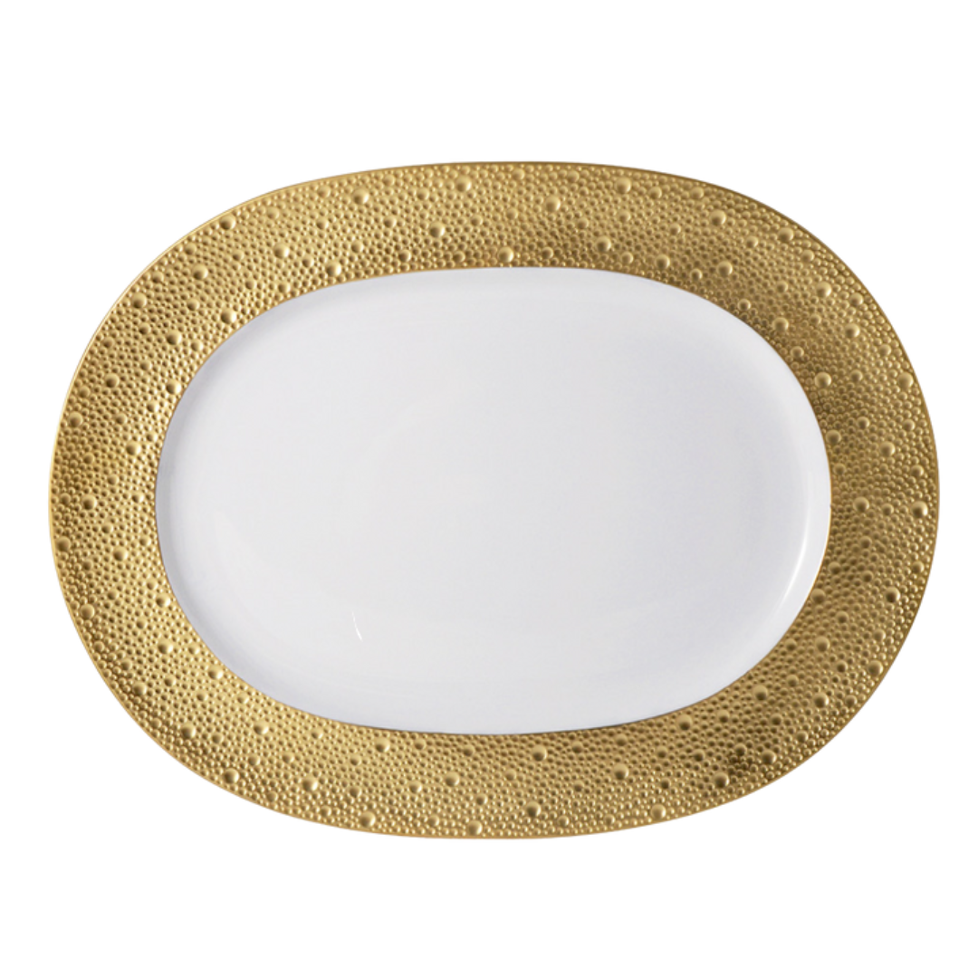 The Bernardaud Ecume Dinnerware Gold plate features an oval shape, a white surface, and a wide, textured gold rim with raised dots for a touch of contemporary elegance.