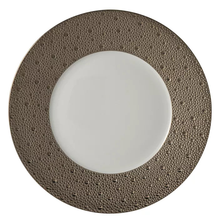 The Bernardaud Ecume Platinum Dinnerware features a round plate with a white center and a wide, textured metallic bronze rim adorned with small raised dots, perfect for modern table settings.