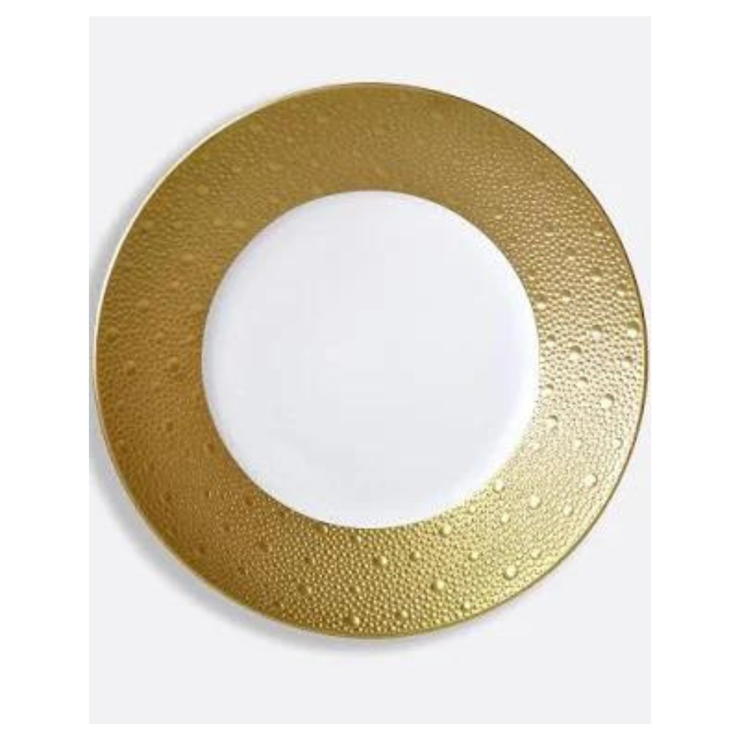 The Bernardaud Ecume Dinnerware Gold is a round white plate with a wide, textured gold rim and dotted pattern, adding contemporary elegance to your table. Shown against a plain light background.