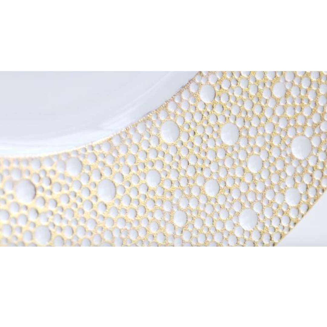 Close-up of a Bernardaud Ecume Dinnerware Mordore plate, showcasing a white surface with an elegant gold and white circular dot pattern along the rim.