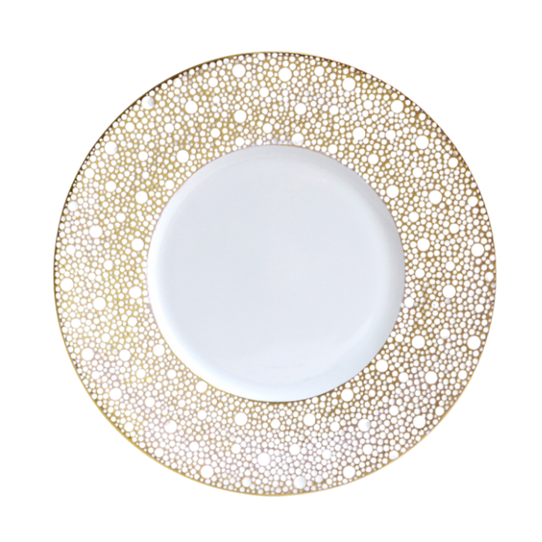 The Bernardaud Ecume Dinnerware Mordore is a white porcelain plate with a wide rim adorned by an intricate gold dot pattern, giving this piece an elegant and decorative look.