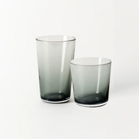 Two translucent charcoal hand-blown glass tumblers—one tall, one short—from Gary Bodker's Everyday Glasses collection are placed side by side on a plain white background.