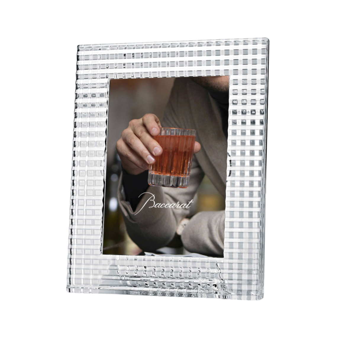 The Baccarat Eye Photo Frame, crafted from clear textured crystal, displays a photo showing only the lower face and hand of a person in a beige sweater holding a glass of red drink, with "Baccarat" written on the image.