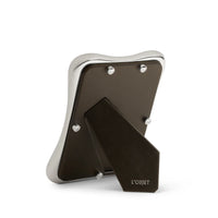 The Anton Frame Platinum by L'Objet is shown from the back, revealing a wavy platinum border, brown stand, and the L'Objet logo on its sturdy base for an added touch of luxury.