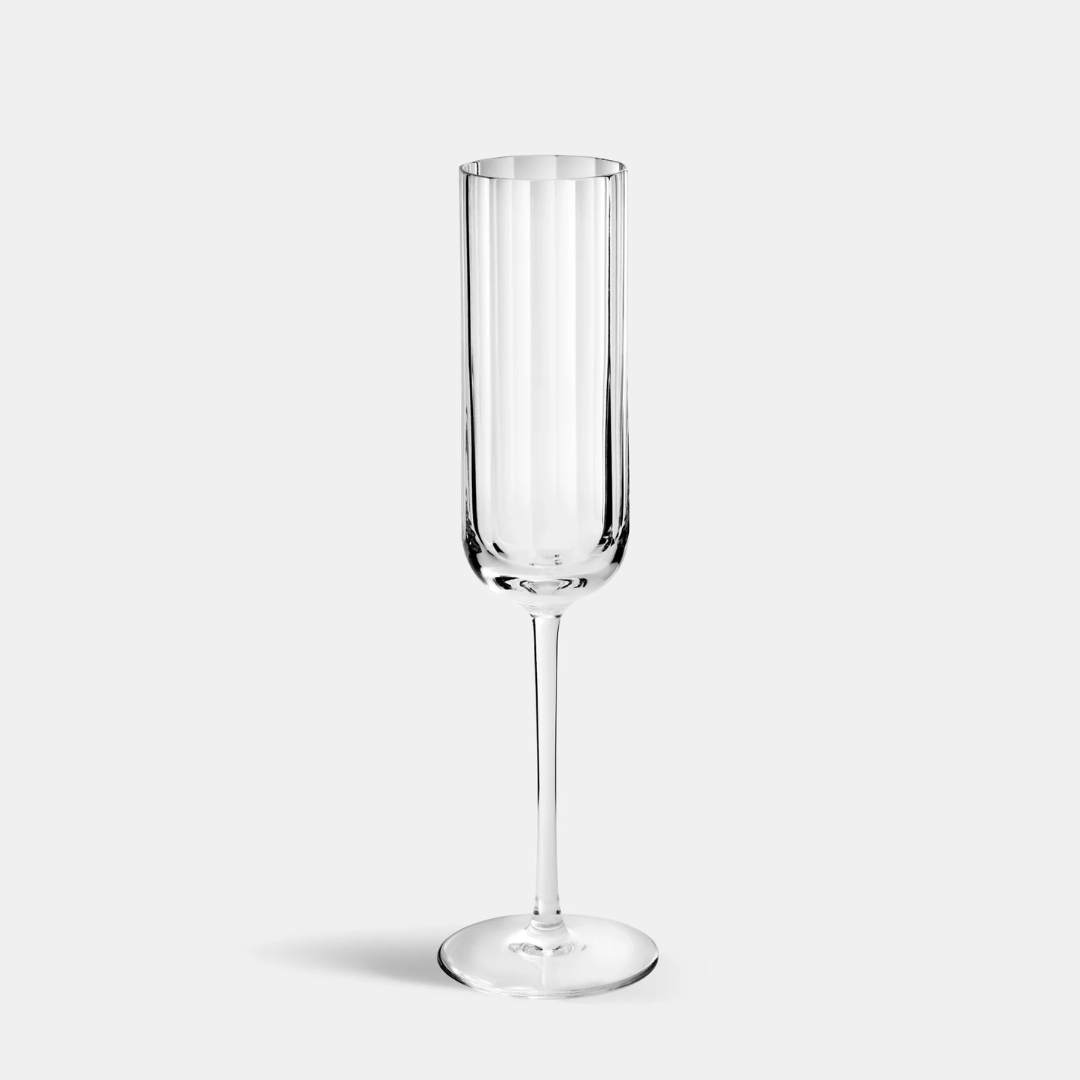 A single Richard Brendon Fluted Champagne Glass with a long stem, inspired by Art Deco style, stands upright on a plain light gray background.