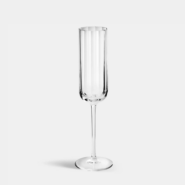 A single Richard Brendon Fluted Champagne Glass with a long stem, inspired by Art Deco style, stands upright on a plain light gray background.