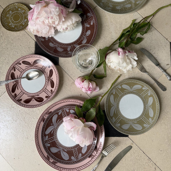 Overhead view of hand-painted Sevilla Dinnerware Brown porcelain plates in brown, pink, and olive green, arranged on a tiled floor with peonies, a glass, and silverware.