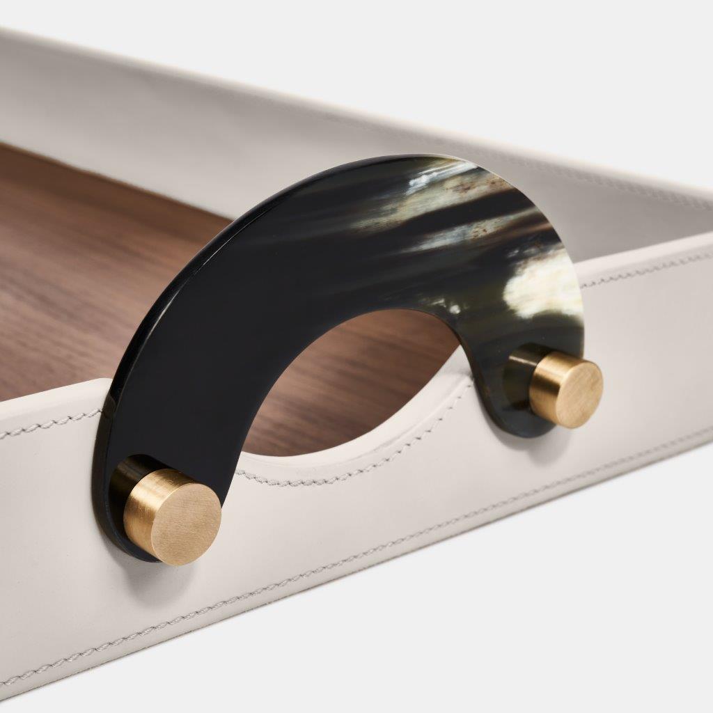 A close-up of the Luho Maeve Rectangle Tray, featuring a luxury leather surface with white stitching, a walnut wooden base, and a curved black handle secured by two round brass fittings.