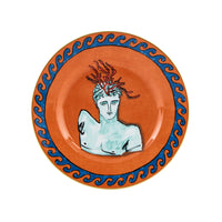 The Ginori 1735 Il Viaggio Di Nettuno Dessert Plate - Rock Orange features a marble bust with red snakes, orange center, and blue wave rim—a striking Medusa-inspired piece from the luxury collection.