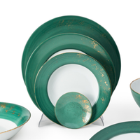 Golden Green Dinnerware by Molecot features hand-painted ceramic plates and bowls with white centers, green rims, and gold splatter accents. This elegant set is displayed upright and overlapping for a stylish presentation.