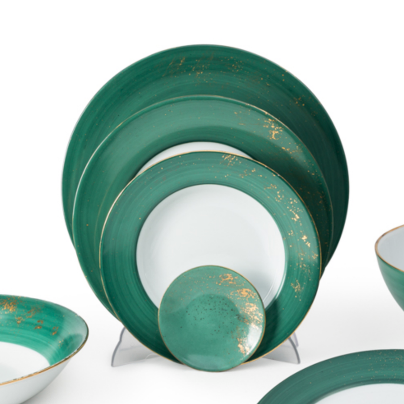 Golden Green Dinnerware by Molecot features hand-painted ceramic plates and bowls with white centers, green rims, and gold splatter accents. This elegant set is displayed upright and overlapping for a stylish presentation.