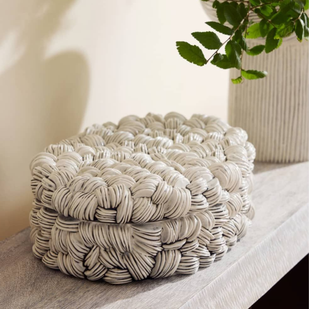 The Arteriors Hampton Box - New Addition, with its intricate looped texture and ice reactive glaze, sits on a wooden surface beside a white vase filled with green leafy branches.