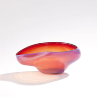 The Harmony Bowl Red - Small by Global Views / Surya is a glossy, abstract handblown art glass piece featuring a flowing, asymmetric shape and gradient colors that blend from orange to red. Set against a plain white background, this handmade bowl exudes individuality and elegance—perfect for modern luxury décor.