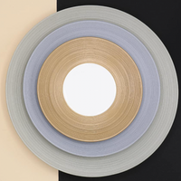 Three concentric circular mats in gold, silver, and gray—evoking JL Coquet’s Hemisphere Dinnerware Grey—are centered over a diagonal beige and black background with a white center.