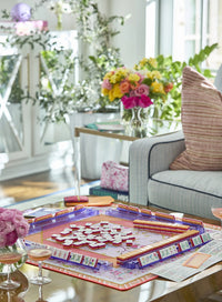 An Oh My Mahjong Mahjong Mats set is displayed with floral tiles, two pink cocktails, and a bouquet of flowers in the background.