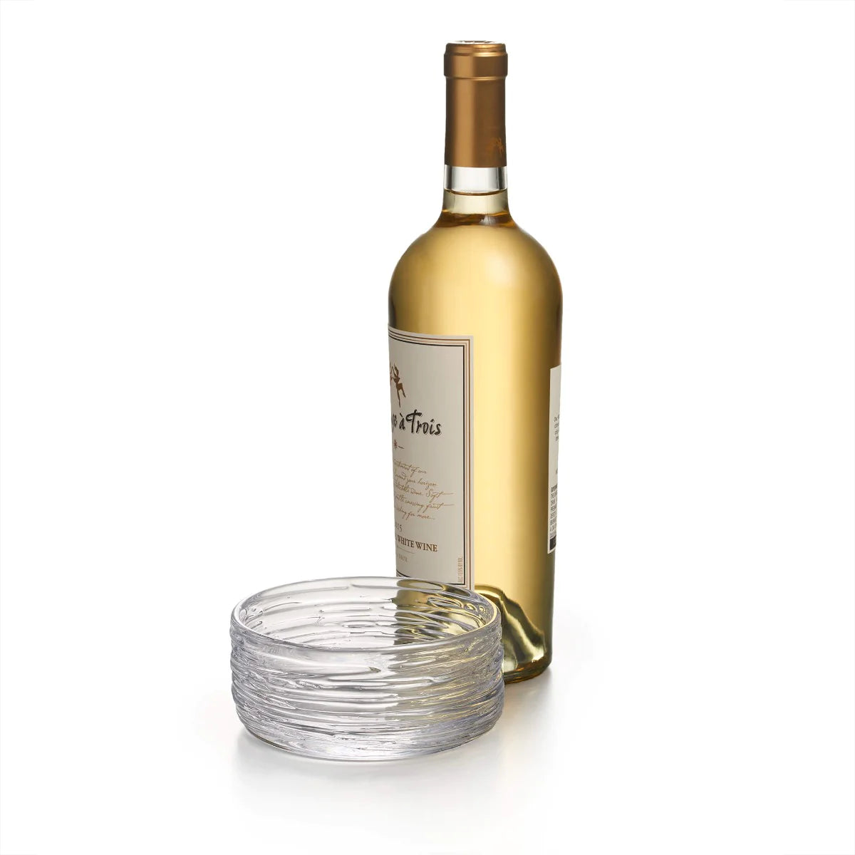 A bottle of white wine with a gold cap stands beside the Simon Pearce Echo Lake Wine Coaster, both set against a white background.