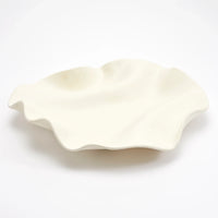 A white, wavy-edged ceramic plate with an irregular, organic shape sits on a plain white background. The Celine Raw Blanc Tray by Dumae is hand-crafted to perfection—an elegant table accessory or a unique centerpiece that brings refined style to any setting.