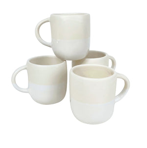Four white Urban Dinnerware ceramic mugs by Alex Marshall Studios, featuring rounded shapes and handles, are stacked in pairs. Their smooth finish complements handmade stoneware plates. These mugs are microwave and dishwasher safe.