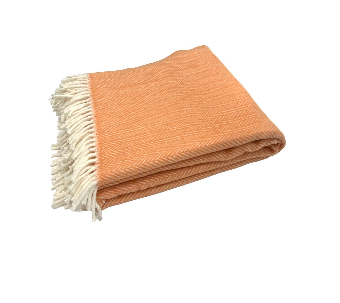 The A Soft Idea Herringbone Plush Throw features a folded orange design with a subtle chevron pattern and white fringed edges; this soft, machine-washable blanket is displayed on a white background for easy care.