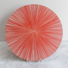 The Tisch New York Lines Placemat Set of 4 features an elegant cork-backed table mat, shown upright on a white marble surface next to a round plate with red and white radial stripes and a starburst effect, against a simple background.