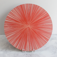 The Tisch New York Lines Placemat Set of 4 features an elegant cork-backed table mat, shown upright on a white marble surface next to a round plate with red and white radial stripes and a starburst effect, against a simple background.