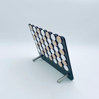 A standing Luxe Dominoes Connect Four El Cuatro board with alternating black and white discs, displayed against a plain white background. The classic four in a row game is supported by two metal legs.