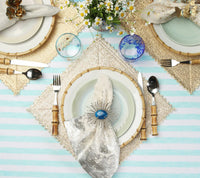 Three place settings on a striped table, each featuring a textured square Kim Seybert Stamped Reversible Placemat Silver & Gold, dinner plates, bamboo-handled silverware, and a napkin held by a decorative ring.