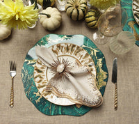 Elegant table setting featuring Kim Seybert’s Fringe Tablecloth in Natural & Silver, gold and green marble-patterned charger, gold-trimmed plate, decorative napkin ring, gold flatware, wine glasses, yellow flowers, and small gourds.