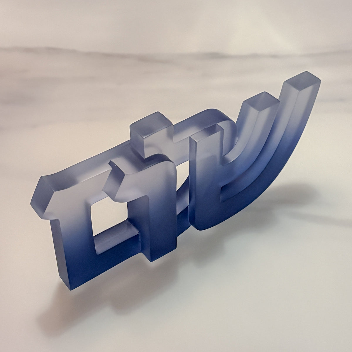 The Shalom Sculpture by CDMX / BRUCI is a translucent blue resin piece with interlocking geometric shapes, displayed on a smooth surface with a soft, blurred background—an elegant accent for modern Jewish home decor.