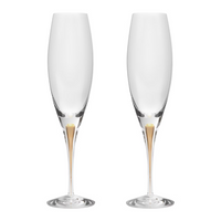The Orrefors Kosta Boda Intermezzo Champagne Glass Gold Set of 2, designed by Erika Lagerbielke from mouth-blown glass, features long stems and a gold accent at the base, shown side by side on a white background.