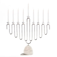 The Coluna Menorah Carrara Marble & Silver by Anna New York features a sleek geometric silver design that holds nine white candles, set atop a refined base of Italian Carrara marble against a plain white background.