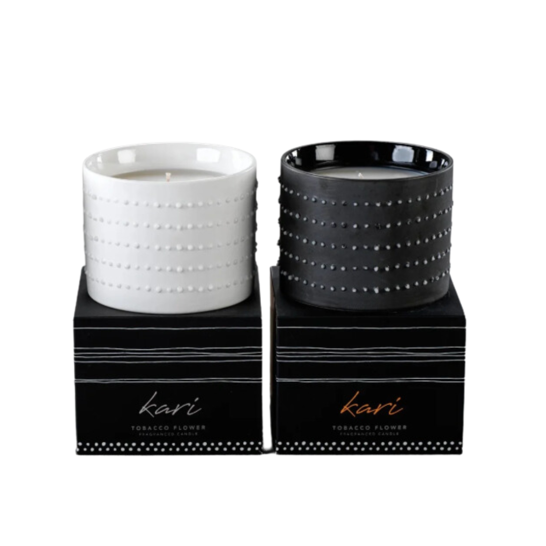 Two ceramic Kari Candles by Zodax, in white and black, sit on sleek black boxes labeled "kari TOBACCO FLOWER." Their minimalist dot and stripe design adds style to any room—ideal for a tobacco vanilla-scented home fragrance.