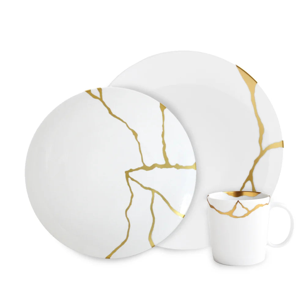 The Bernardaud Kintsugi Dinnerware set includes a dinner plate, salad plate, and mug in white Limoges porcelain, each accented with gold kintsugi-inspired lines for a refined look.