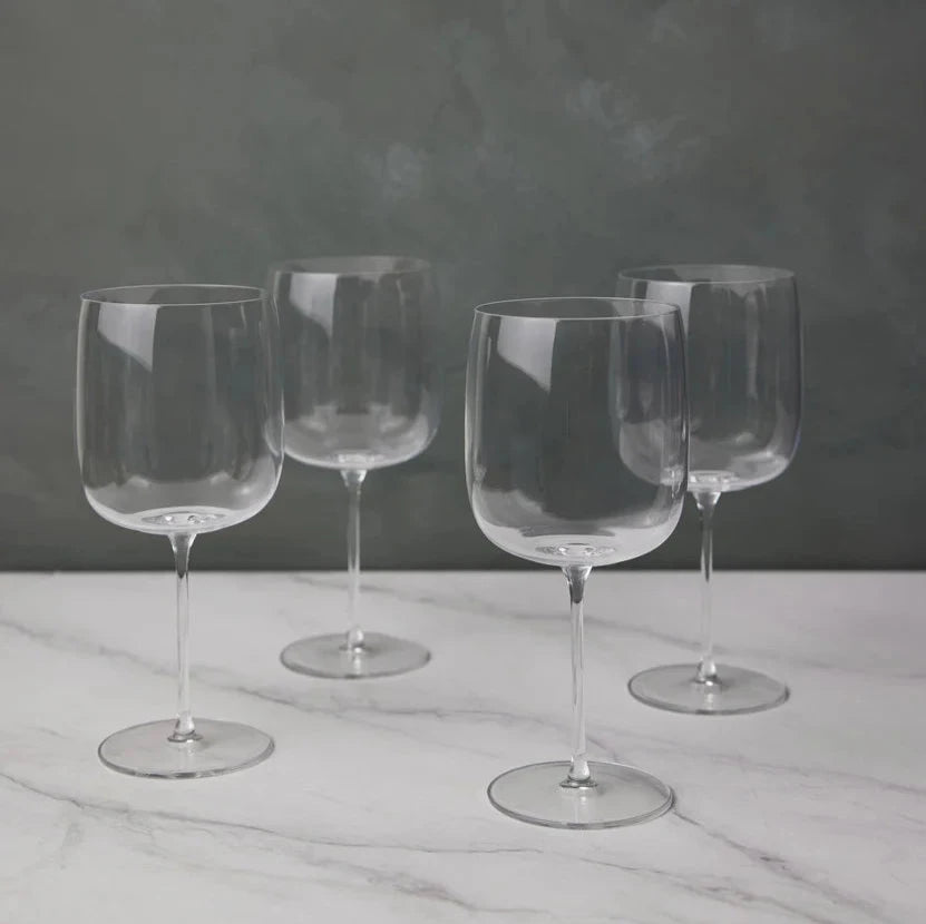 Four empty, clear Borough Barware glasses by LSA are arranged on a white marble surface with a gray textured background. Their reflections add elegance, making this Set of 4 a stylish addition to any barware collection.