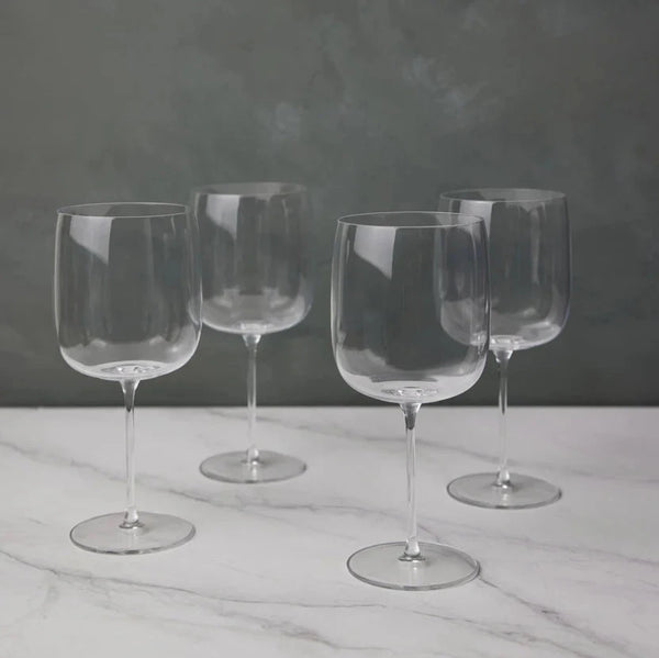 Four empty, clear Borough Barware glasses by LSA are arranged on a white marble surface with a gray textured background. Their reflections add elegance, making this Set of 4 a stylish addition to any barware collection.