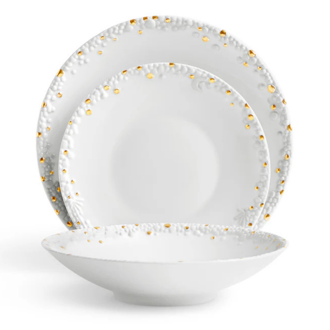 Three white Haas Mojave Dinnerware Gold pieces by L'Objet—each with embossed patterns and gold dot accents—are arranged: a dinner plate at the back, salad plate in the middle, and a shallow bowl at the front.