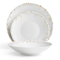 Three white Haas Mojave Dinnerware Gold pieces by L'Objet—each with embossed patterns and gold dot accents—are arranged: a dinner plate at the back, salad plate in the middle, and a shallow bowl at the front.