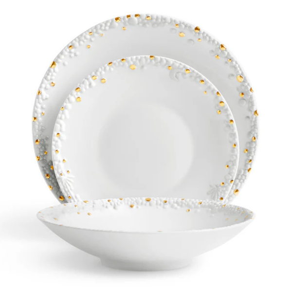 Three white Haas Mojave Dinnerware Gold pieces by L'Objet—each with embossed patterns and gold dot accents—are arranged: a dinner plate at the back, salad plate in the middle, and a shallow bowl at the front.