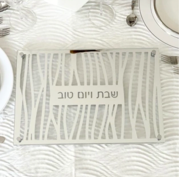 The BT-Shalom Lazer Cut Challah Board Pearl & Silver features Hebrew text "שבת ויום טוב" in the center, displayed on a white tablecloth set for an elegant Shabbat meal.